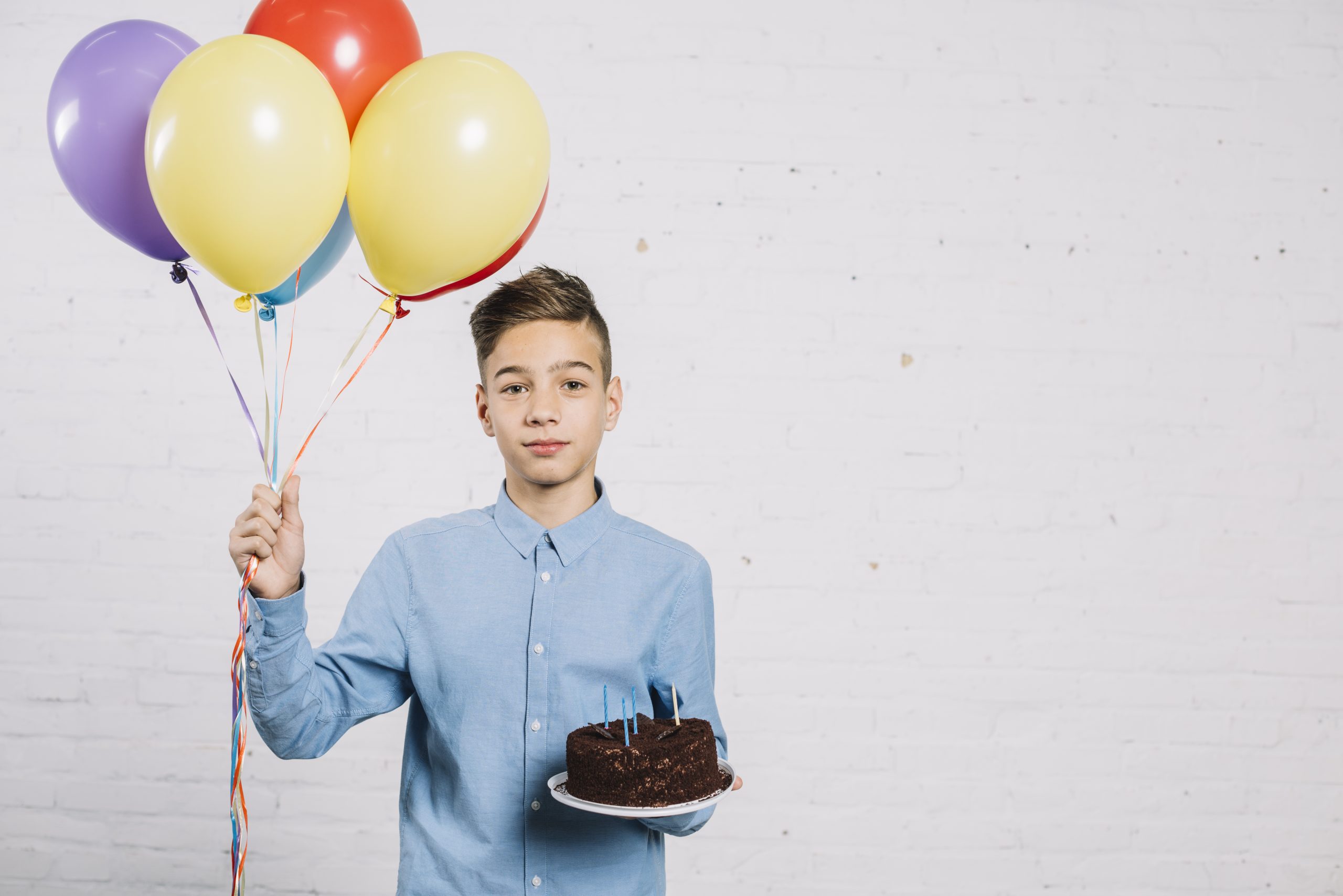 portrait teenage boy holding balloons birthday cake against wall scaled