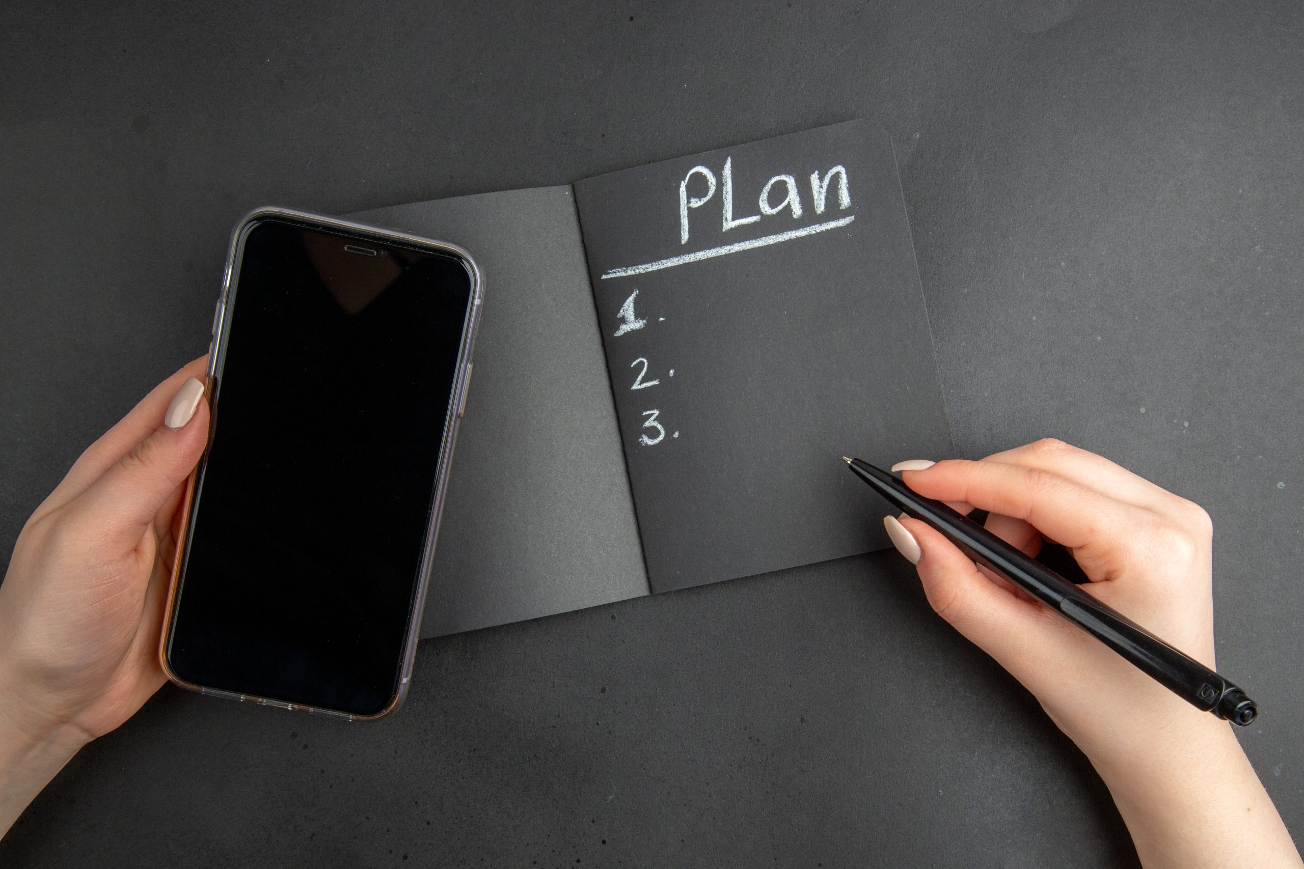 top view plan written black notepad phone pen female hands black background scaled